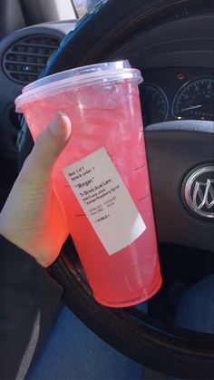 a hand holding a plastic cup with a label on it sitting in the drivers seat of a car