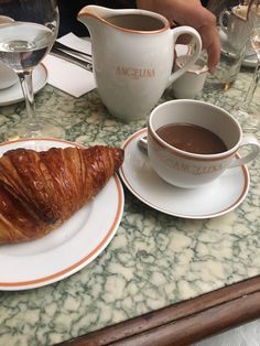 a croissant on a plate next to a cup of coffee and saucer