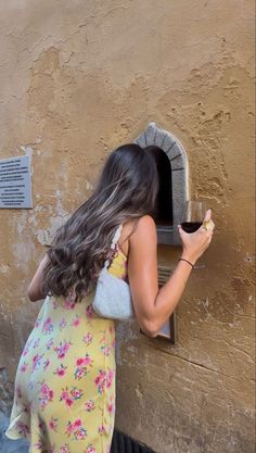 a woman in a yellow dress is looking into a brick wall with a small window