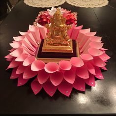 a small buddha statue sitting on top of a table next to pink paper flowers and doily