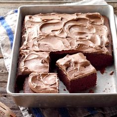 a pan filled with brownies and frosting on top of a wooden table next to a towel