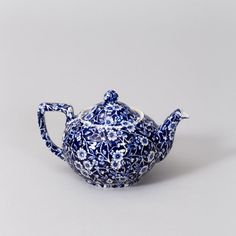 a blue and white porcelain teapot with flowers on it's lid, sitting against a gray background