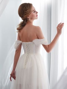 a woman in a white wedding dress looking out the window with her hand on her hip