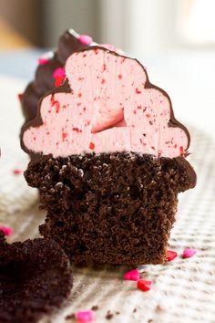 two chocolate cupcakes with pink frosting and sprinkles on a table