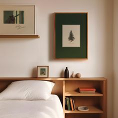 a bed with white sheets and pillows in a bedroom next to two framed pictures on the wall