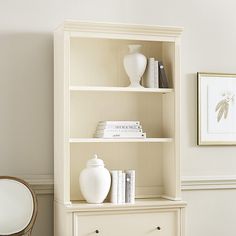 a white book shelf with books and vases on it in the corner of a room