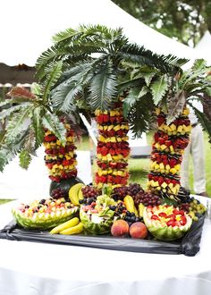 a table topped with lots of fruit and palm trees on top of a white table cloth