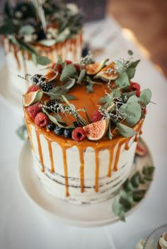 two cakes decorated with fruit and greenery on top of a white tablecloth covered table