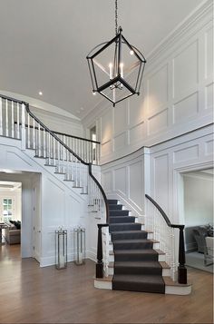 a staircase in a house with white walls and wood flooring, chandelier hanging from the ceiling