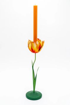 an orange and red flower sitting on top of a green base next to a candle