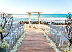 an outdoor wedding setup with white chairs and flowers on the aisle leading to the beach