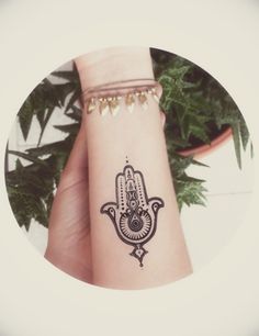 a small hamsa tattoo on the wrist is shown in front of a potted plant