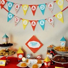 a red table topped with lots of desserts next to bunting and paper flags