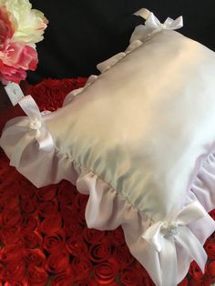 a white pillow with ruffles and bows on it next to a pink flower