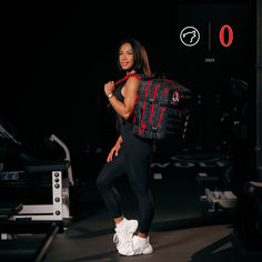 a woman is standing in the dark with a gym bag on her back and smiling