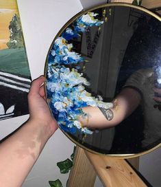 a person holding up a mirror with flowers on it