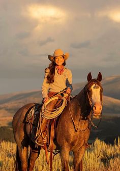 a woman wearing a cowboy hat sitting on top of a brown horse in a field