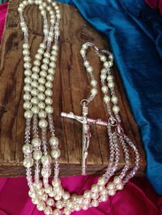 a necklace with white pearls and a cross hanging from it's end on a wooden board