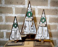 three wooden christmas trees sitting on top of a table next to a brick wall with a wreath