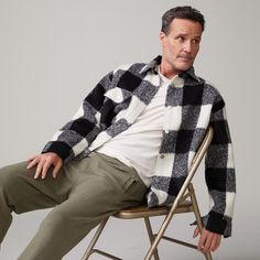 Front view of model sitting in chair wearing the plaid flannel jacket in black, natural check. Classic Plaid Outerwear With Relaxed Fit, Black Relaxed Fit Shacket For Winter, Classic Black Long Sleeve Shacket, Classic Black Shacket For Winter, Classic Black Winter Shacket, Shacket Men, Mens Flannel Jacket, Fall Flannel Shirt, Mens Plaid Flannel