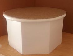 a round white box with a brown top on a wooden table next to a wall