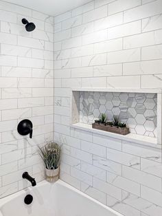 a white tiled bathroom with black fixtures and plants in the window sill above the bathtub