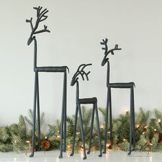 three metal deer sculptures sitting on top of a white floor next to evergreen branches and pine cones