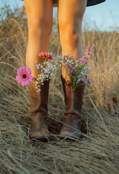 the legs of a woman wearing cowboy boots with flowers in their booties on top of dry grass