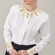 "Indulge in timeless glamour with our White Cotton Shirt adorned with Golden Embroidery Details. This elegant festive blouse is a statement piece crafted to elevate your ensemble effortlessly. Designed with meticulous attention to detail, it features hidden button placket and subtly padded shoulders, offering a refined silhouette that exudes sophistication. KEY FEATURES: - Luxurious white cotton fabric - Intricate golden embroidery details for a touch of opulence - Hidden buttons placket for a sleek finish - Subtly padded shoulders for added structure and elegance - Suitable for women size S - M - Excellent vintage condition - Dry clean only Fabric Information: 100% cotton MEASUREMENTS (while lying flat): Armpit to armpit: 52 cm | 20.5\" Length: 67 cm | 26.4\" Sleeves: 57 cm | 22.4\" Shoul Elegant Workwear Tops With Embellished Collar, Elegant Tops With Embellished Collar For Work, Spring Formal Tops With Embellished Collar, Elegant Formal Shirt With Embellished Collar, Spring Formal Top With Embellished Collar, Formal Spring Top With Embellished Collar, Elegant Fitted Top With Embellished Collar, Embroidered Long Sleeve Formal Tops, Embroidered Long Sleeve Tops For Formal Occasions