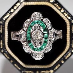 an antique diamond and emerald ring sits in a black box with gold trimmings