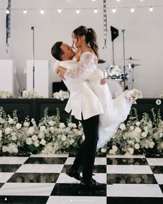 a bride and groom kissing in front of a checkered floor with flowers on it