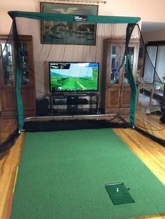 an indoor golf simulator is set up in a room with wood floors and green carpet