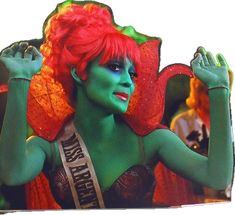 a woman with red hair and green make - up is posing for the camera while holding her hands behind her head