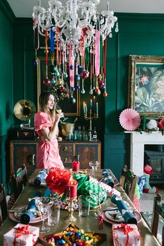 a woman standing in front of a dining room table with presents on it and decorations hanging from the ceiling