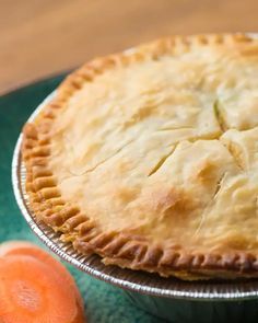 a pie sitting on top of a green plate next to sliced carrots and a knife