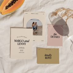 various wedding stationery items laid out on top of a white tablecloth with fruit and paper