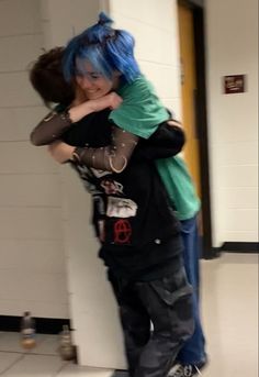 two people with blue hair hugging each other in a hallway, one person has her arms around the other's head