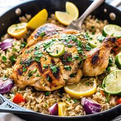 a skillet with chicken and rice topped with lemons, red onions, lime wedges and cilantro