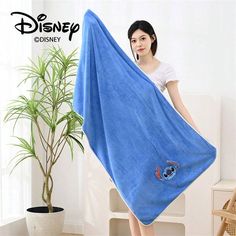 a woman holding up a blue towel in front of a potted plant with disney character on it