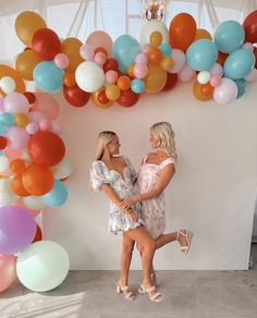 two women standing next to each other in front of balloons