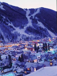 the town is lit up at night in the snow covered mountainside with trees and buildings