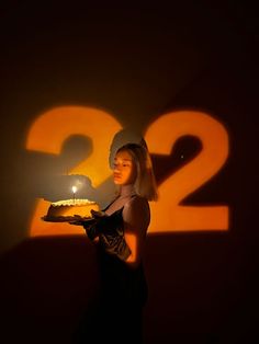 a woman holding a cake in front of a number two sign with the candle lit