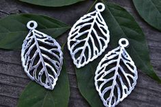 three metal leaf charms sitting on top of leaves