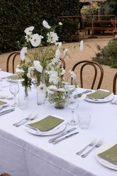 the table is set with white flowers and green napkins on it, along with silverware