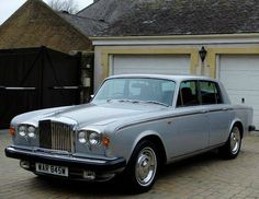 an old silver car parked in front of a house with two garage doors on the side