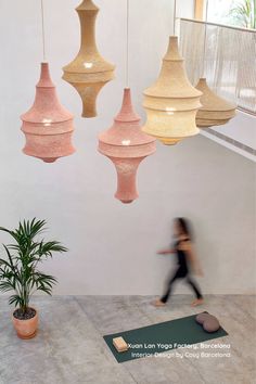 a woman is walking in front of some hanging light fixtures and a potted plant