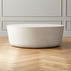 a large white bowl sitting on top of a wooden floor in front of a wall