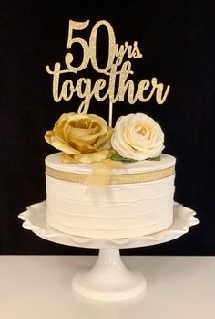 a white cake with gold ribbon and flowers on top that says 50 years together in cursive letters