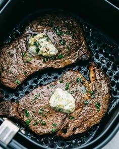 two steaks cooking in an air fryer with butter and chives on top