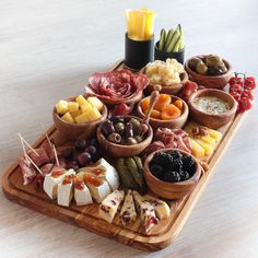 an assortment of cheeses and meats on a wooden platter with olives